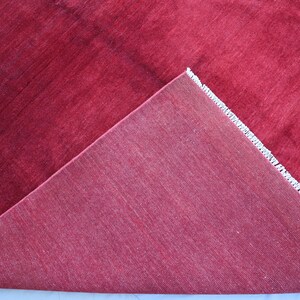 May include: Close-up of a red rug with a white fringe. The rug is folded in half, showing the underside.