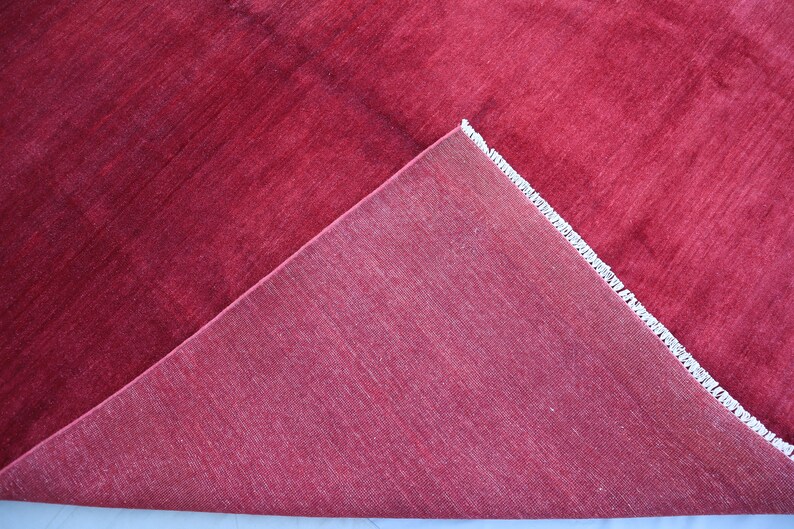 May include: Close-up of a red rug with a white fringe. The rug is folded in half, showing the underside.