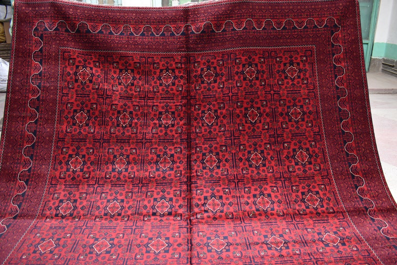 May include: A red rug with a traditional Persian design. The rug has a dark blue border with a white pattern. The center of the rug is filled with a repeating pattern of stars and geometric shapes.
