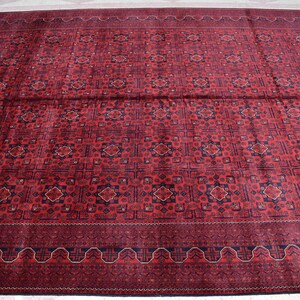 May include: A red rug with a geometric pattern in shades of blue and cream. The rug has a border with a repeating design.