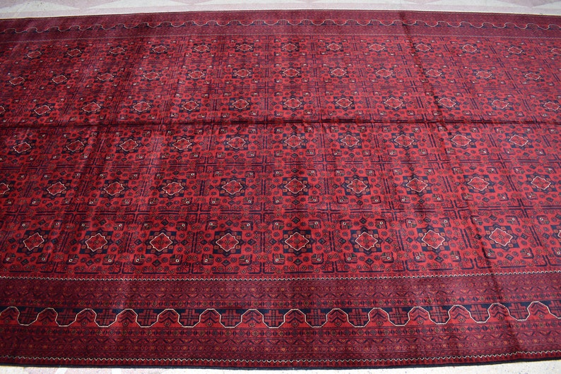 May include: A red rug with a geometric pattern in shades of blue and cream. The rug has a border with a repeating design.