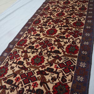 May include: A rectangular rug featuring a beige background with a repeating pattern of red, brown, and dark blue geometric shapes and floral motifs. The rug has a dark blue border with star-like designs. The rug is likely made of wool.