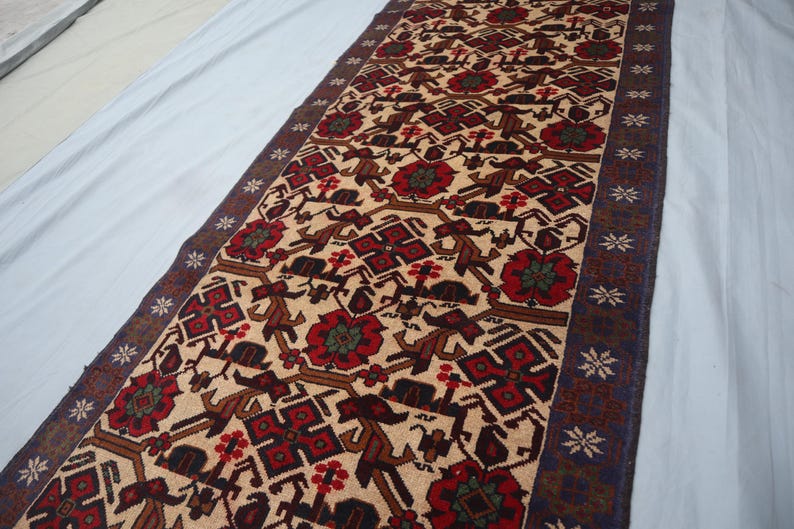 May include: A rectangular rug featuring a beige background with a repeating pattern of red, brown, and dark blue geometric shapes and floral motifs. The rug has a dark blue border with star-like designs. The rug is likely made of wool.