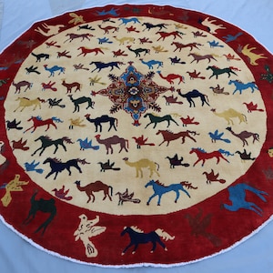 May include: A round rug with a cream background and a red border. The rug features a repeating pattern of stylized horses, camels, and birds in various colors.