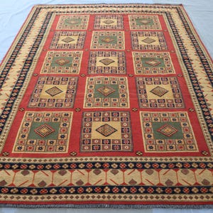 May include: A red, green and beige patterned rug with a geometric design. The rug has a black border with a repeating pattern.