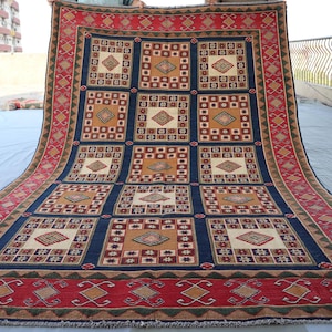May include: A traditional Persian rug with a geometric pattern in shades of red, blue, beige, and brown. The rug has a central medallion and a border with intricate designs.
