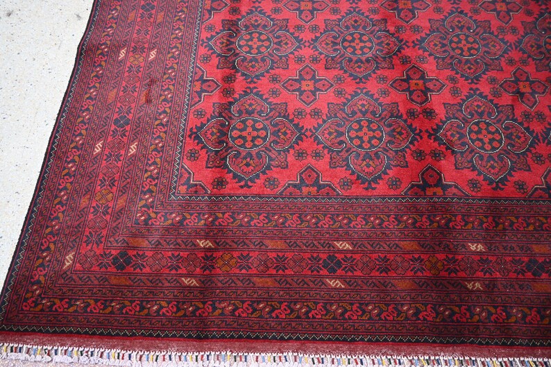 Puede incluir: Una alfombra roja con un patr&oacute;n geom&eacute;trico en blanco y negro. La alfombra tiene un borde con flecos.