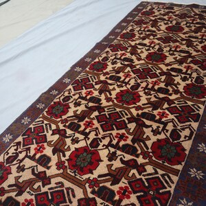 May include: A rectangular rug featuring a beige field with a repeating pattern of red flowers, brown geometric shapes, and dark brown borders. The rug has a dark blue border with white star-like designs.
