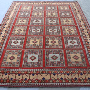 May include: A red, beige and blue patterned rug with a geometric design. The rug has a border with a repeating pattern of leaves and flowers.