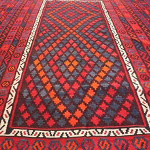 Pu&ograve; includere: Un grande tappeto rettangolare con un motivo a diamante centrale in rosso, arancione e blu. Il bordo presenta disegni geometrici in rosso, nero e bianco. La combinazione di colori del tappeto &egrave; prevalentemente rossa.