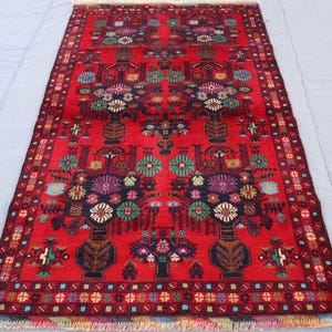 May include: A rectangular red rug with a floral design. The rug features a central pattern of vases filled with colourful flowers, surrounded by a detailed border. The rug's dimensions are approximately 152 cm by 91 cm.