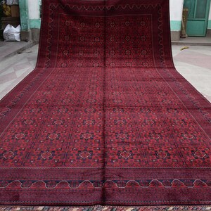 May include: A large, red rug with a intricate geometric pattern in shades of blue and cream. The rug has a thick, plush pile and a fringed border.