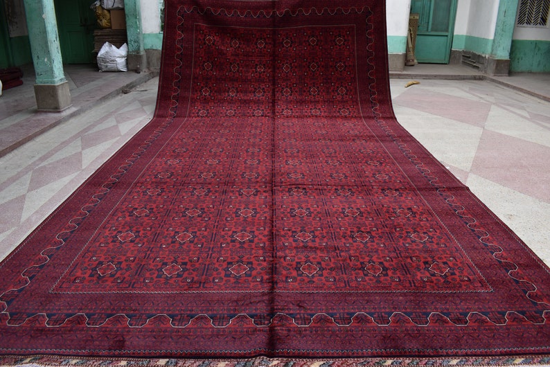 May include: A large, red rug with a intricate geometric pattern in shades of blue and cream. The rug has a thick, plush pile and a fringed border.