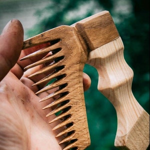 May include: A wooden comb with a long, curved handle. The comb is made of light brown wood and has a natural finish. The handle is made of a darker wood and has a smooth, polished finish.