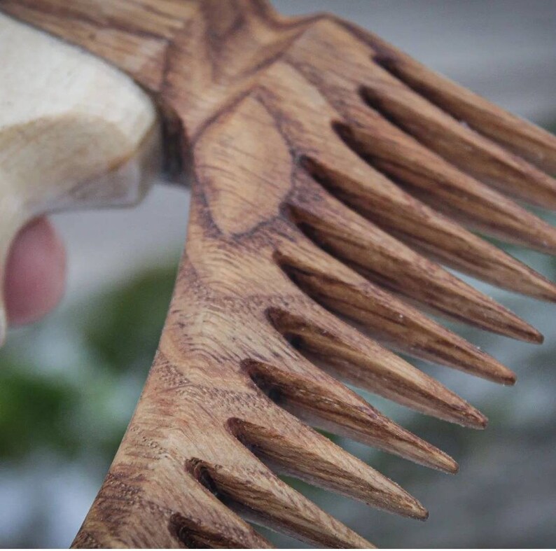 May include: A wooden comb with a curved handle and a row of closely spaced teeth. The comb is made of dark brown wood with a natural grain pattern.