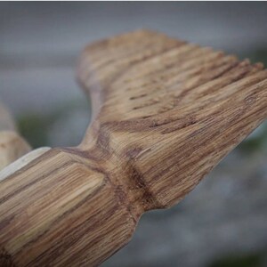 May include: Close-up of a wooden comb with a natural wood grain finish. The comb has a rounded handle and a row of teeth.