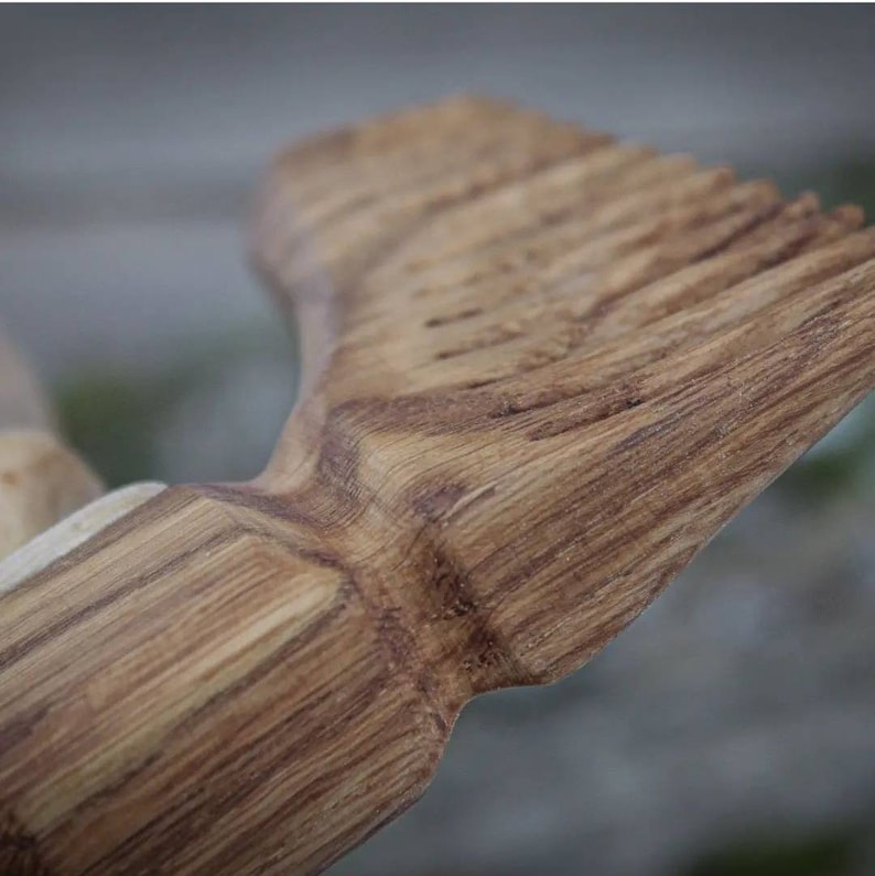 May include: Close-up of a wooden comb with a natural wood grain finish. The comb has a rounded handle and a row of teeth.