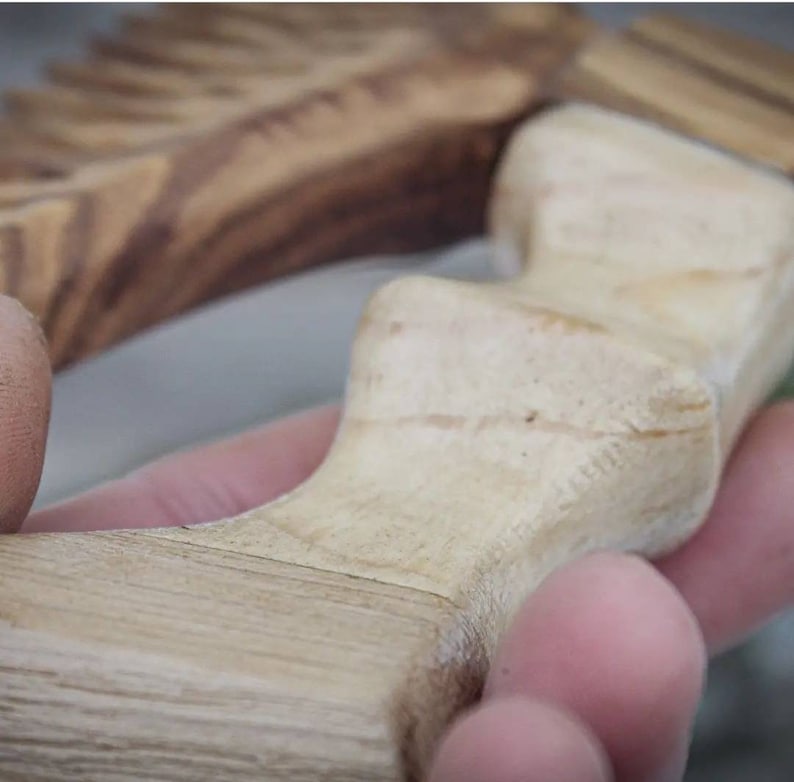 May include: Close-up of a wooden handle with a light brown color and a smooth, polished finish. The handle has a unique, curved shape with a series of ridges.