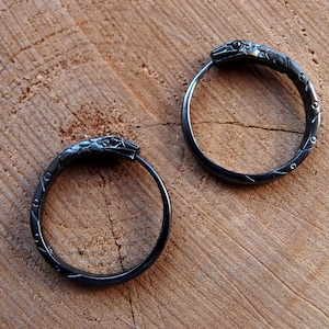 May include: A pair of black hoop earrings with a snake head design. The earrings are made of metal and have a smooth, polished finish.
