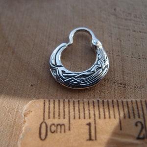 May include: A silver hoop earring with a Celtic knot design. The earring is about 1 cm in diameter.