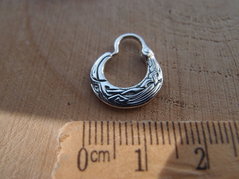 May include: A silver hoop earring with a Celtic knot design. The earring is about 1 cm in diameter.