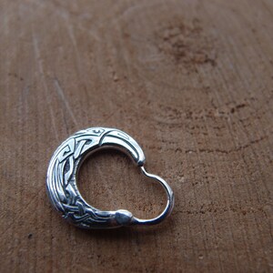 May include: A silver hoop earring with a detailed Celtic knot design. The knotwork features a stylized bird or animal head.