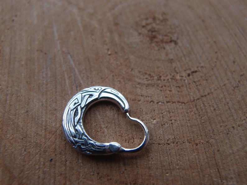 May include: A silver hoop earring with a detailed Celtic knot design. The knotwork features a stylized bird or animal head.