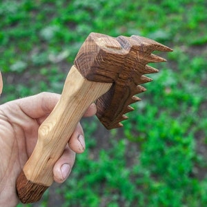 May include: A wooden hand-carved tool with a handle and a comb-like head. The tool is made of light and dark wood.