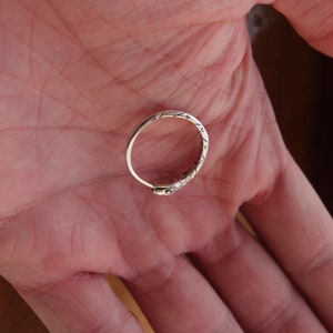 May include: A silver ring with an intricate design. The ring is on a person's hand.
