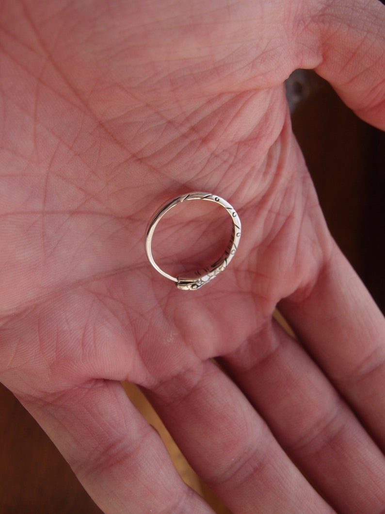 May include: A silver ring with an intricate design. The ring is on a person's hand.