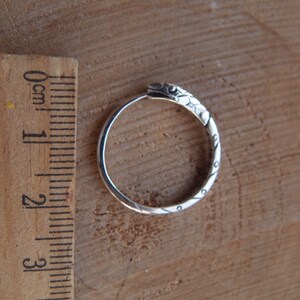 May include: Silver hoop earrings featuring a snake design. The snake is detailed with scales and has a textured finish.