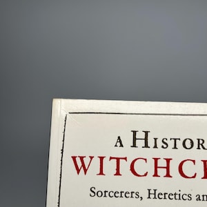 Op de afbeelding: Boekomslag met de titel "A History of Witchcraft" in zwarte en rode letters. De ondertitel luidt "Sorcerers, Heretics and Pagans". De omslag heeft een witte achtergrond met een zwarte rand.