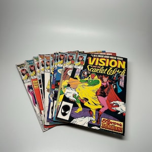 May include: A collection of vintage Marvel comic books, featuring the Vision and Scarlet Witch. The comics display vibrant colors and illustrations, with titles and issue numbers visible. The covers showcase various characters and action scenes.