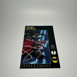 May include: A comic book cover featuring Spawn and Batman against a backdrop of blue lightning. The cover has the title "Spawn Batman" at the top and "Image Comics" at the bottom. The artwork is in a dynamic, action-oriented style.