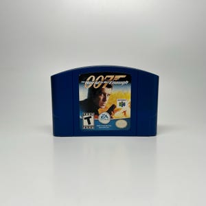 May include: A blue Nintendo 64 game cartridge for "007: The World Is Not Enough." The game's label features a portrait of a man holding a gun, with the game's title and logo at the top. The ESRB rating is "T" for Teen.