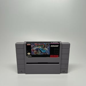 May include: A gray Super Nintendo game cartridge for "Teenage Mutant Ninja Turtles IV: Turtles in Time." The cartridge features a colorful game cover with the game title and the Konami logo.