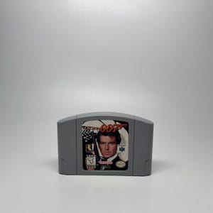 May include: A gray Nintendo 64 video game cartridge for GoldenEye 007. The label features a portrait of a man in a suit holding a firearm, with the red text 007, the Nintendo 64 logo, a Rare logo, and an ESRB Teen rating symbol clearly visible.