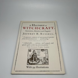 Op de afbeelding: Boek 'A History of Witchcraft' van Jeffrey B. Russell. De omslag is cr&egrave;mekleurig met zwarte tekst en illustraties. De titel van het boek, de auteur en citaten uit recensies worden weergegeven. Het boek bevat 94 illustraties.