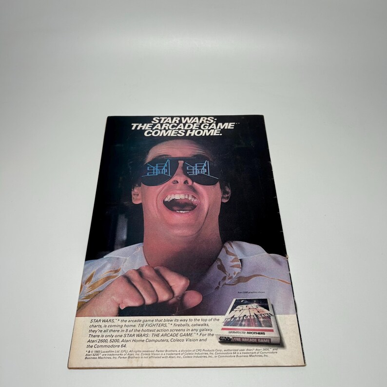Puede incluir: Un anuncio vintage del videojuego dom&eacute;stico Star Wars: The Arcade Game. La imagen muestra a una persona con gafas de sol que reflejan el juego, con el texto STAR WARS: THE ARCADE GAME COMES HOME impreso en la parte superior.