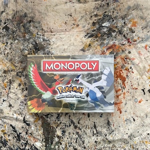 May include: A white ceramic mug with a black handle and the text "But First, Coffee" in a bold, black font. The mug is set against a blurred background, suggesting a cozy setting.