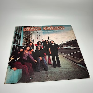 May include: Vintage vinyl record album cover featuring the band Lynyrd Skynyrd. The album cover shows a group of musicians posing on a sidewalk. The album title is displayed in a stylized font with the band's name.