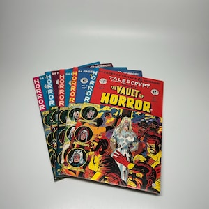 May include: A stack of vintage comic books with the title "The Vault of Horror" in bold letters. The covers feature colorful illustrations of monsters and horror themes. The comics are in various colors, including red, blue, and green.
