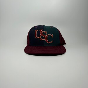 May include: A maroon, navy blue, and green baseball cap with a gold embroidered "USC" logo.