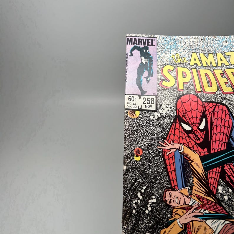 Puede incluir: Un c&oacute;mic vintage de Marvel titulado The Amazing Spider-Man n&uacute;mero 258, con fecha de noviembre. La portada muestra a un personaje con traje rojo y azul sobre una persona con chaqueta beige, con una figura negra en el recuadro superior.