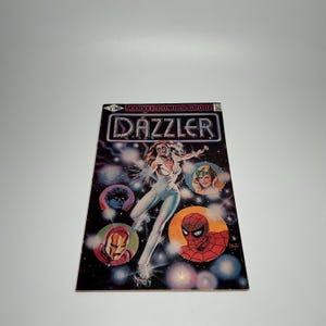 May include: A vintage comic book titled "Dazzler" from Marvel Comics Group. The cover features a woman in a white jumpsuit, surrounded by colorful illustrations of other characters. The background is a dark space with stars.