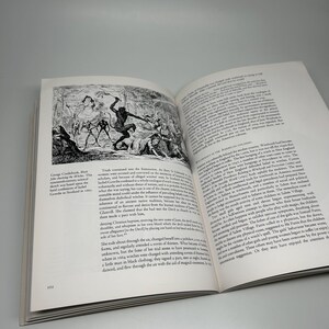 Op de afbeelding: Een open boek met een zwart-wit illustratie die een historische sc&egrave;ne weergeeft, mogelijk een heksenproces. Tekst op de pagina bespreekt hekserij in de Amerikaanse koloni&euml;n. Het paginanummer 102 is zichtbaar.
