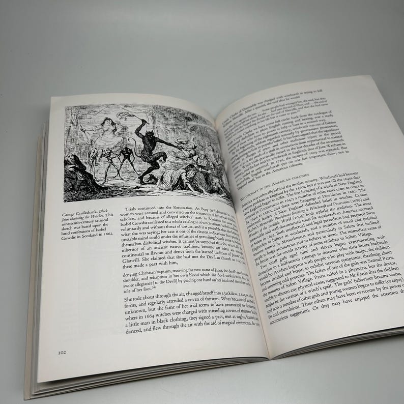 Op de afbeelding: Een open boek met een zwart-wit illustratie die een historische sc&egrave;ne weergeeft, mogelijk een heksenproces. Tekst op de pagina bespreekt hekserij in de Amerikaanse koloni&euml;n. Het paginanummer 102 is zichtbaar.