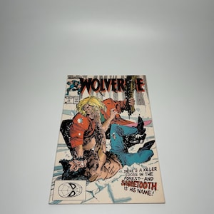 May include: A comic book cover featuring Wolverine in a fight scene. The cover has the title "Wolverine" in large letters. The artwork depicts two figures in combat, with text that reads "THERE'S A KILLER LOOSE IN THE FOREST--AND SABRETOOTH IS HIS NAME!"