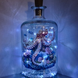 May include: A clear glass bottle with a cork stopper and a printed image of an octopus in a coral reef setting. The bottle is filled with white fairy lights.
