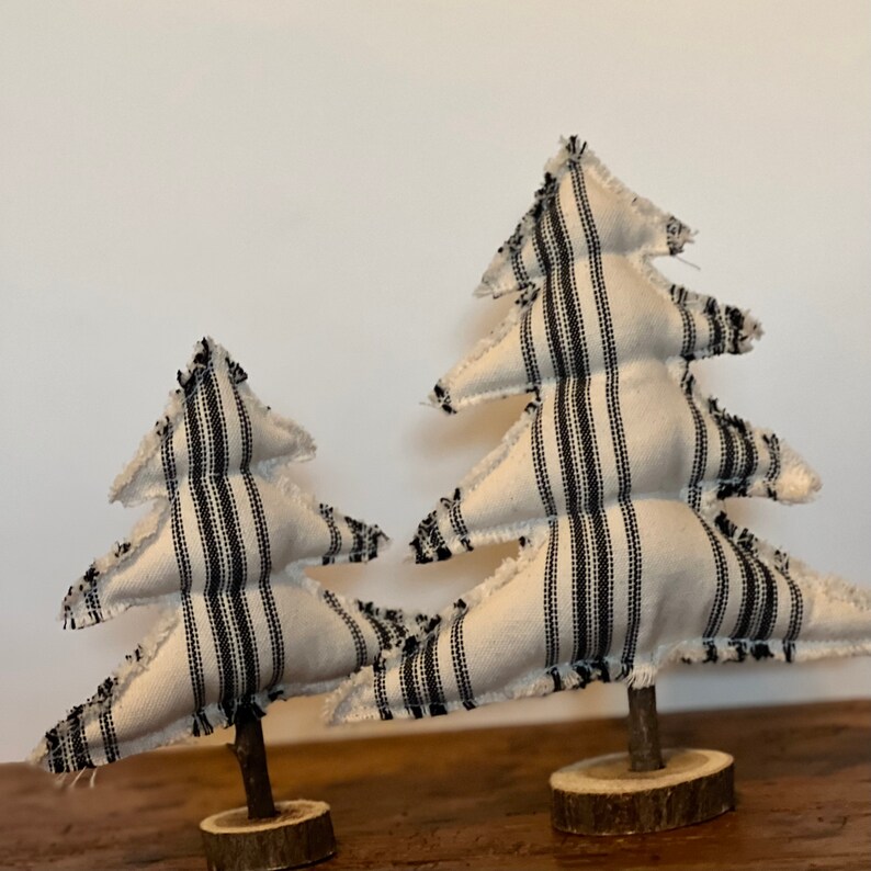 Pu&ograve; includere: Due piccoli alberi di Natale in tessuto bianco con strisce nere. Gli alberi sono su basi di legno.